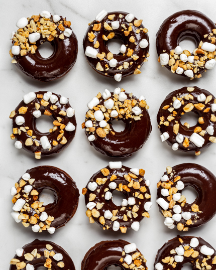 Une douzaine de beignes au chocolat avec glaçage au chocolat saupoudrés d’arachides et de guimauves