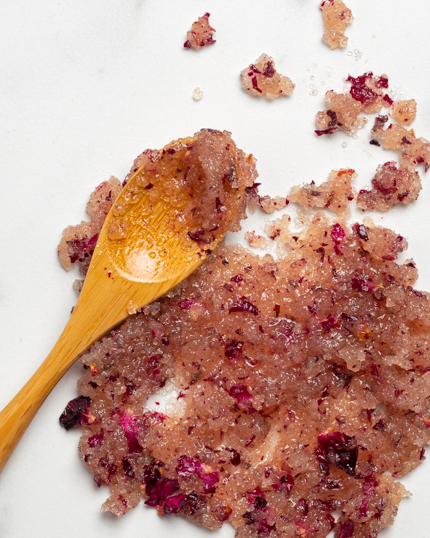 Pétales de rose et exfoliant au sucre biologique et à l’eau de rose avec une cuillère de bois.