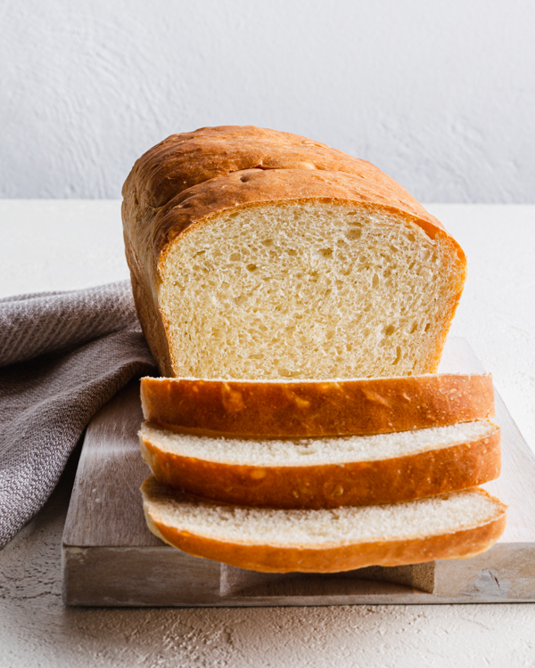 Une miche de pain sur une planche à découper, avec trois tranches déjà coupées