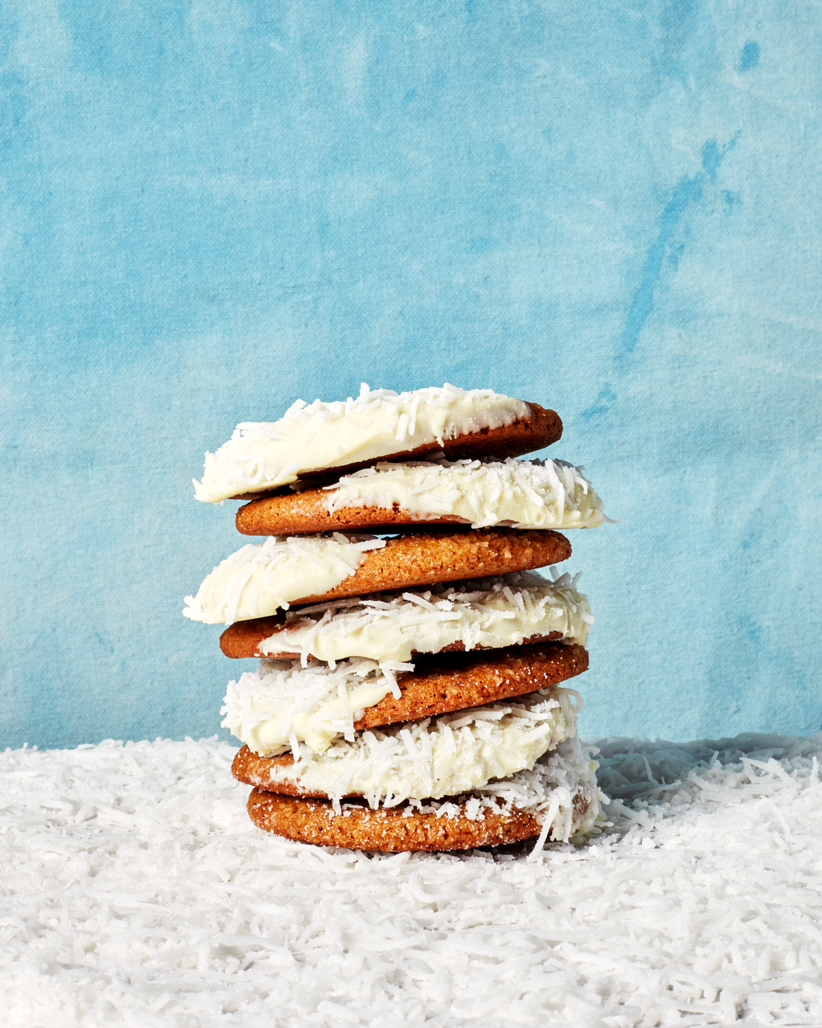  Une pile de biscuits au gingembre à moitié trempés dans le chocolat blanc et de la noix de coco sur un lit de noix de coco râpée, devant un fond hivernal