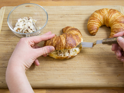 Farcir l’incision du croissant avec du fromage de chèvre, sur une planche à découper