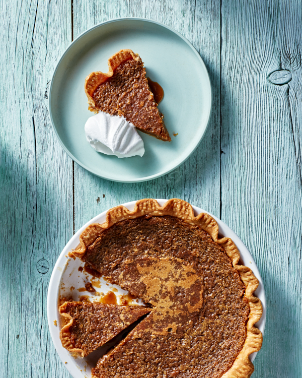 Une tarte au sucre dans un moule à tarte blanc avec deux pointes coupées, dont une pointe servie dans une assiette bleu pâle avec une quenelle de crème fouettée.