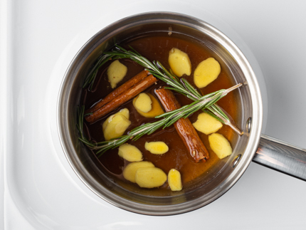 Sur une cuisinière, une casserole avec du sirop simple, du romarin, du gingembre et des bâtons de cannelle