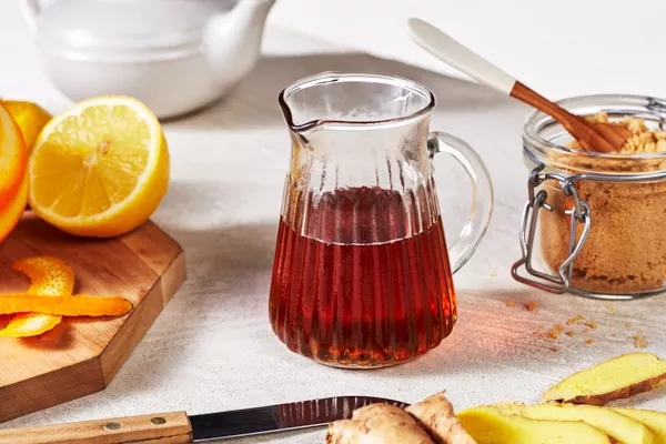 Un bol en verre octogonal de yaourt et de granola garni de sirop de gingembre sucré et épicé présenté avec une tasse en verre de sirop, un bol de granola et une cuillère à mélanger.