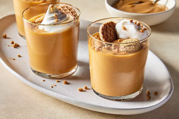 Trois verres de pudding au caramel écossais sur un petit plateau ovale, chacun garni de crème fouettée, de morceaux de toffee et de biscuits. 