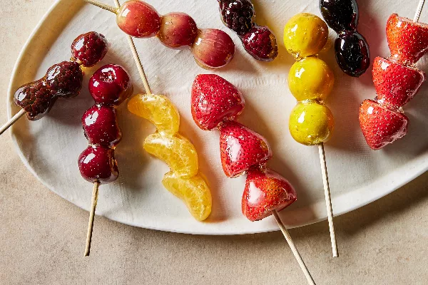 Un plateau de fruits et de baies en brochettes enrobés de sirop de sucre clair, ou tanghulu, incluant des segments de mandarine, des cerises, des raisins, des groseilles à maquereau, des fraises, des kumquats et des mûres.