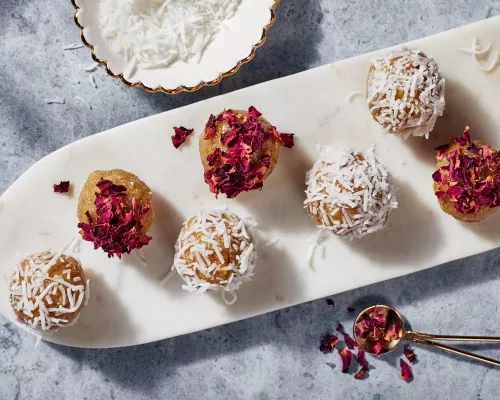 Laddo badam dorés garnis de pétales de rose et de morceaux de noix de coco sur une fine assiette blanche