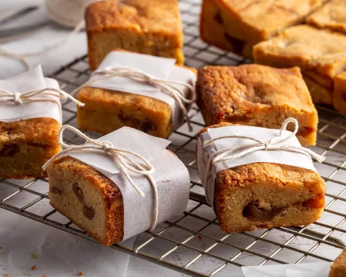 Des blondies aux pommes qui refroidissent sur une grille et d’autres emballés dans du papier parchemin