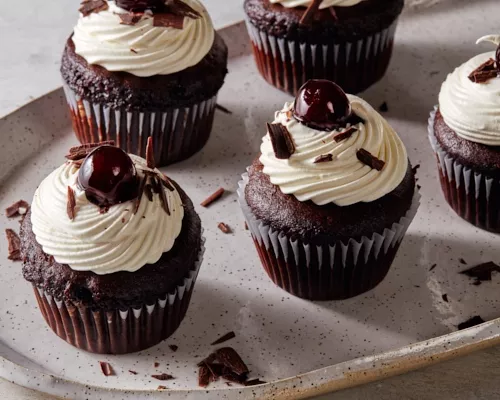 Cinq petits gâteaux Forêt Noire avec glaçage chantilly, garnis de cerises et de copeaux de chocolat sur un plateau.