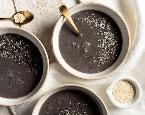 Trois bols de soupe au sésame noir avec garniture de graines de sésame blanches et noires, placés sur une table en bois