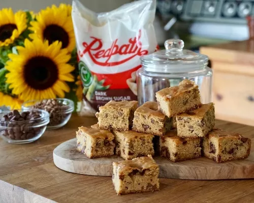 Blondies au beurre noisette avec pépites de chocolat disposés sur un comptoir de type bloc de boucher avec des tournesols