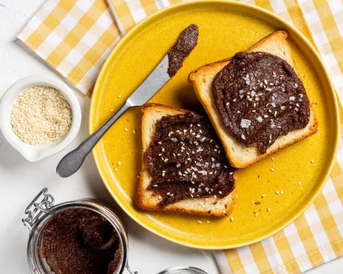 Deux rôties garnies de tartinade cacao et tahini sur une assiette jaune avec un couteau