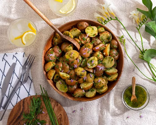 Salade de pommes de terre à l’aneth dans un bol en bois sur une nappe et un verre de limonade