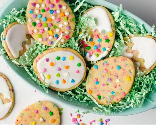 Six biscuits en forme d’œufs de Pâques décorés avec des confettis et du glaçage royal, dans un panier