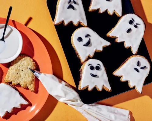 Tartelettes en forme de fantômes, certaines décorées avec des visages en glaçage noir sur du glaçage blanc