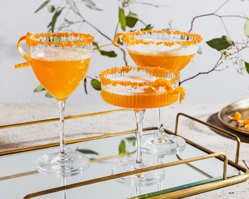 Trois verres de cocktail pétillant au gingembre et au curcuma garnis d'écorces d'orange et bordés de sucre