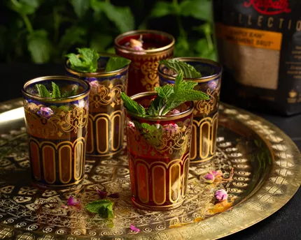 Cinq verres colorés remplis de thé marocain à la menthe, décorés de feuilles de menthe et disposés sur un plateau doré