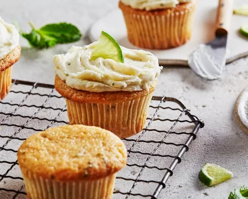 Cupcakes style mojito sur une grille de refroidissement, certains garnis d'un glaçage à l'hermine et garnis de citron vert.