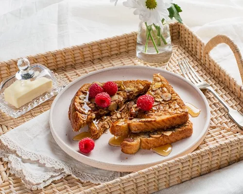 Pain doré croustillant avoine et amandes sur un plateau de service en rotin, du beurre sous une cloche en verre et des fleurs da