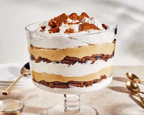 Un gâteau au fromage au potiron de taille familiale dans un grand bol en verre à pied avec des biscuits émiettés sur le dessus.