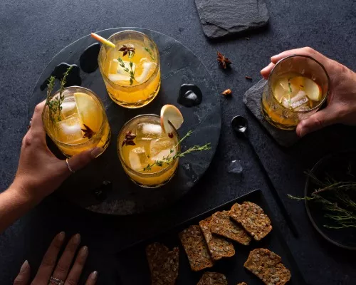 Mains approchant des verres de cocktail à la pomme et aux épices pour tarte à la citrouille servies avec des craquelins