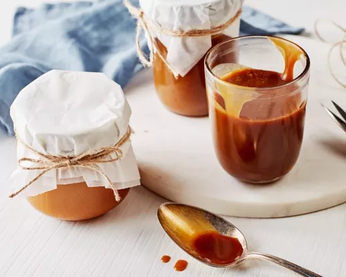 Trois bocaux en verre de sauce au caramel salé, l'un ouvert et les deux autres recouverts d'un tissu et fermés par une ficelle.