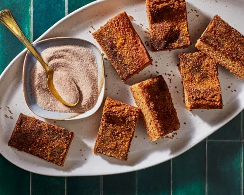 Sept barres de biscuits snickerdoodle sur un plateau blanc avec un plat de sucre à la cannelle et une cuillère dorée