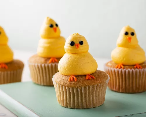 Cupcakes avec poussins jaunes faits de glaçages sur une planche verte en bois