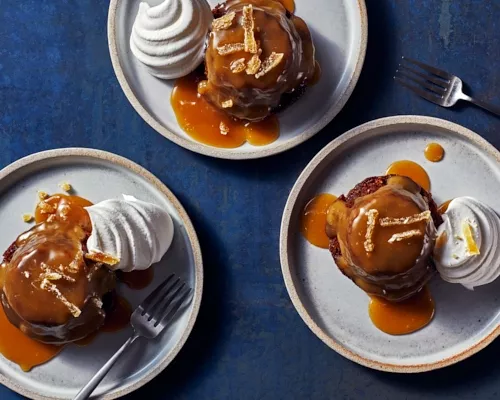 Vue de haut en bas de trois sticky toffee puddings sur des assiettes, chacun avec une cuillerée de crème fouettée et de sauce