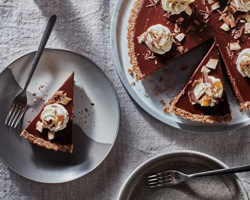 Tarte au chocolat chai végétalien sans cuisson sur un plateau avec deux tranches coupées, une servie sur une assiette