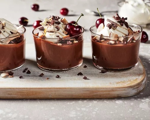 Deux puddings au chocolat végétaliens garnis de crème fouettée, de flocons de noix de coco, de flocons de cacao et de cerises.