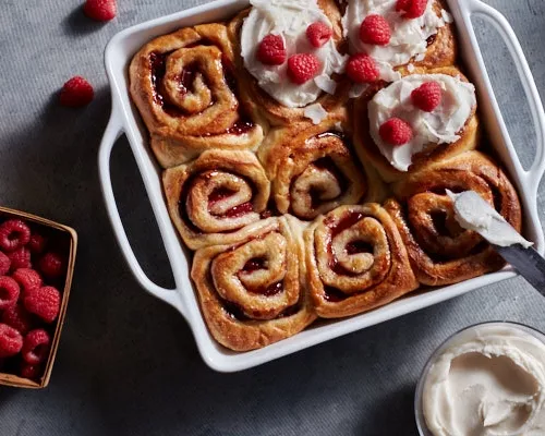Petits pains frais végétaliens à la cannelle  et aux framboises dans un plat à four, certains sans glaçage, d'autres avec un gla