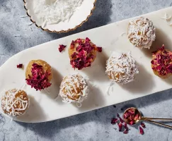 Laddo badam dorés garnis de pétales de rose et de morceaux de noix de coco sur une fine assiette blanche