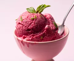 Un bol rose de yogourt glacé aux petits fruits garni de feuilles de basilic