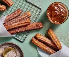 Churros avec du sucre à la cannelle sur une grille de refroidissement avec une trempette de dulce de leche.