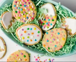 Six biscuits en forme d’œufs de Pâques décorés avec des confettis et du glaçage royal, dans un panier