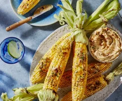 Épis de maïs grillés avec un bol de beurre au chipotle et au citron vert, accompagnés d'un verre d'eau glacée avec lime