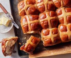 Brioches de carême sur une plaque de cuisson, dont un a été retiré, tranché et beurré