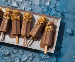 Sucettes de kulfi au chocolat avec des noisettes hachées, fondant dans un plateau