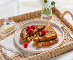 Pain doré croustillant avoine et amandes sur un plateau de service en rotin, du beurre sous une cloche en verre et des fleurs da