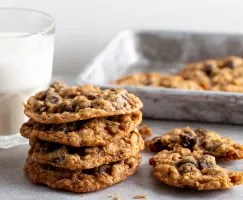 Une pile de biscuits aux flocons d'avoine et aux pépites de chocolat avec un verre de lait et un plateau de service en métal.