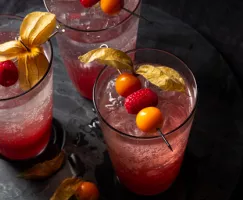 Trois verres de shrub framboises et groseilles avec eau pétillante, décorés de framboises et de groseilles