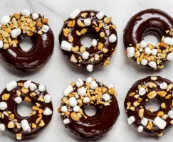 Un beigne au chocolat avec glaçage au chocolat, à moitié saupoudré d’arachides et de guimauves, auquel il manque une bouchée