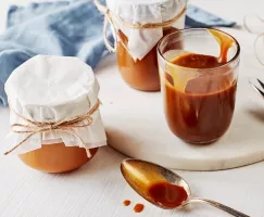 Trois bocaux en verre de sauce au caramel salé, l'un ouvert et les deux autres recouverts d'un tissu et fermés par une ficelle.