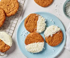 Des biscuits au gingembre à moitié trempés dans le chocolat blanc et de la noix de coco sur une assiette bleue et sur une grille