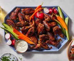 Un plateau d’ailes de poulet grillées sucrées et épicées accompagnées de crudités, d’une trempette et de boissons pétillantes