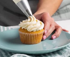  Une femme glaçant un cupcake à la vanille à l’aide d’une poche à pâtisserie avec une pointe en métal