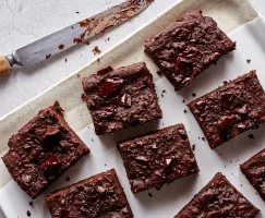 Des brownies végétaliens garnis de morceaux de chocolat noir sur un plateau avec un couteau.